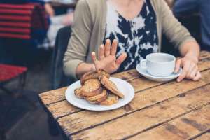 Woman sitting a table with her hand up pushing away a plate of toast stories you hear