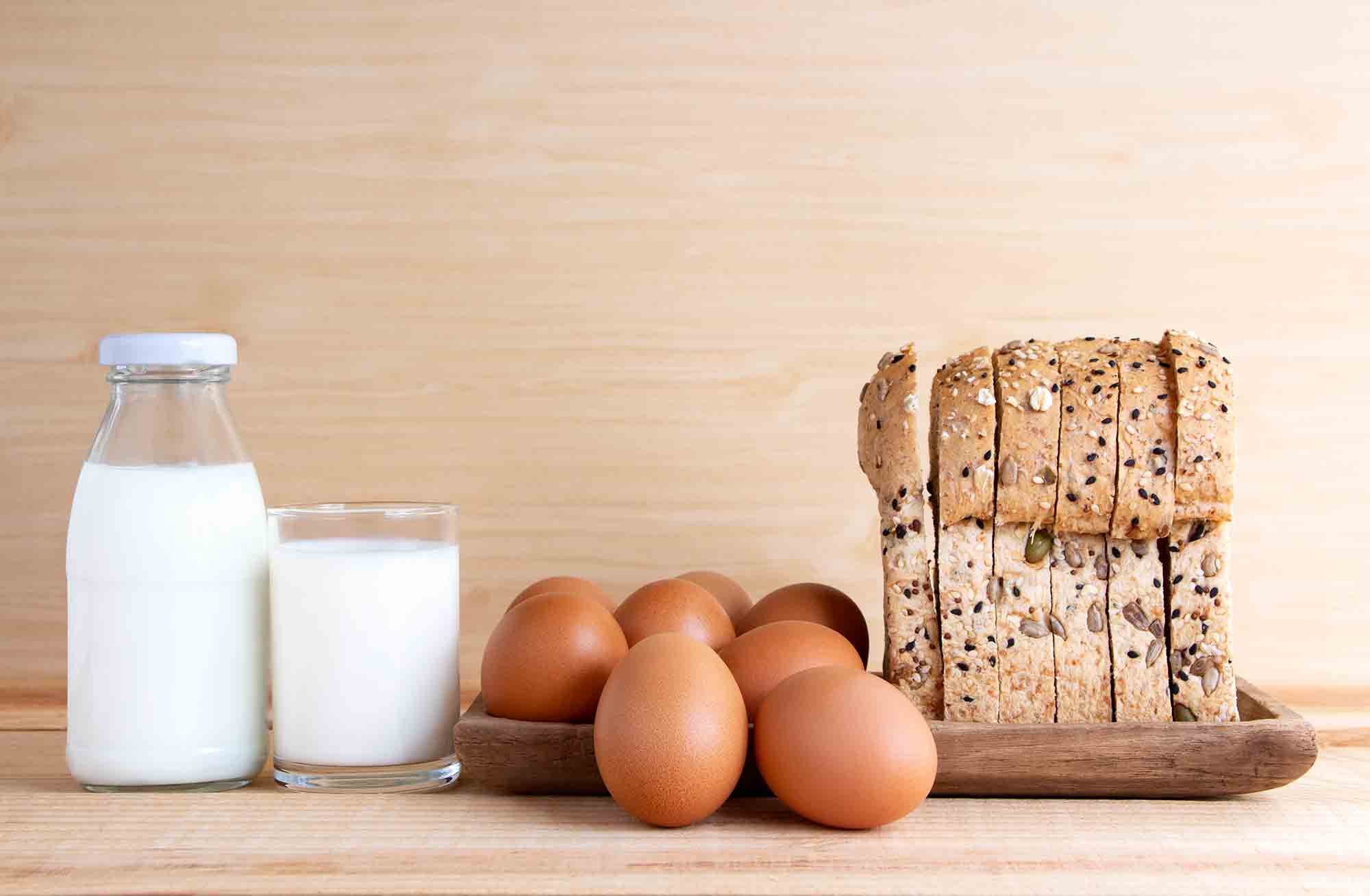 Jar and glass or milk, several brown egg and a six slices of bread on a plate on a wooden table egg allergies
