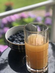 glass of kombucha with a bowl of blueberries behind it