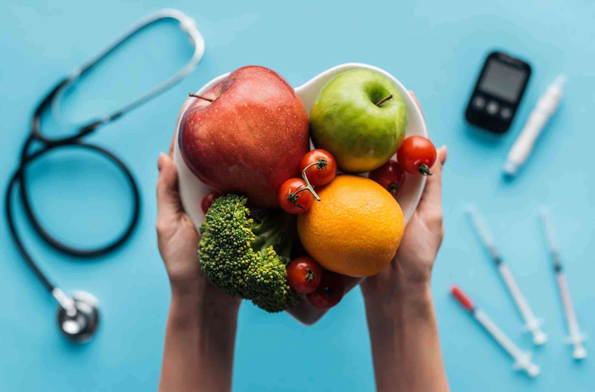 fruits-and-vegetables-in-female-hands-with-medical-equipment-on-blue-background diabetes