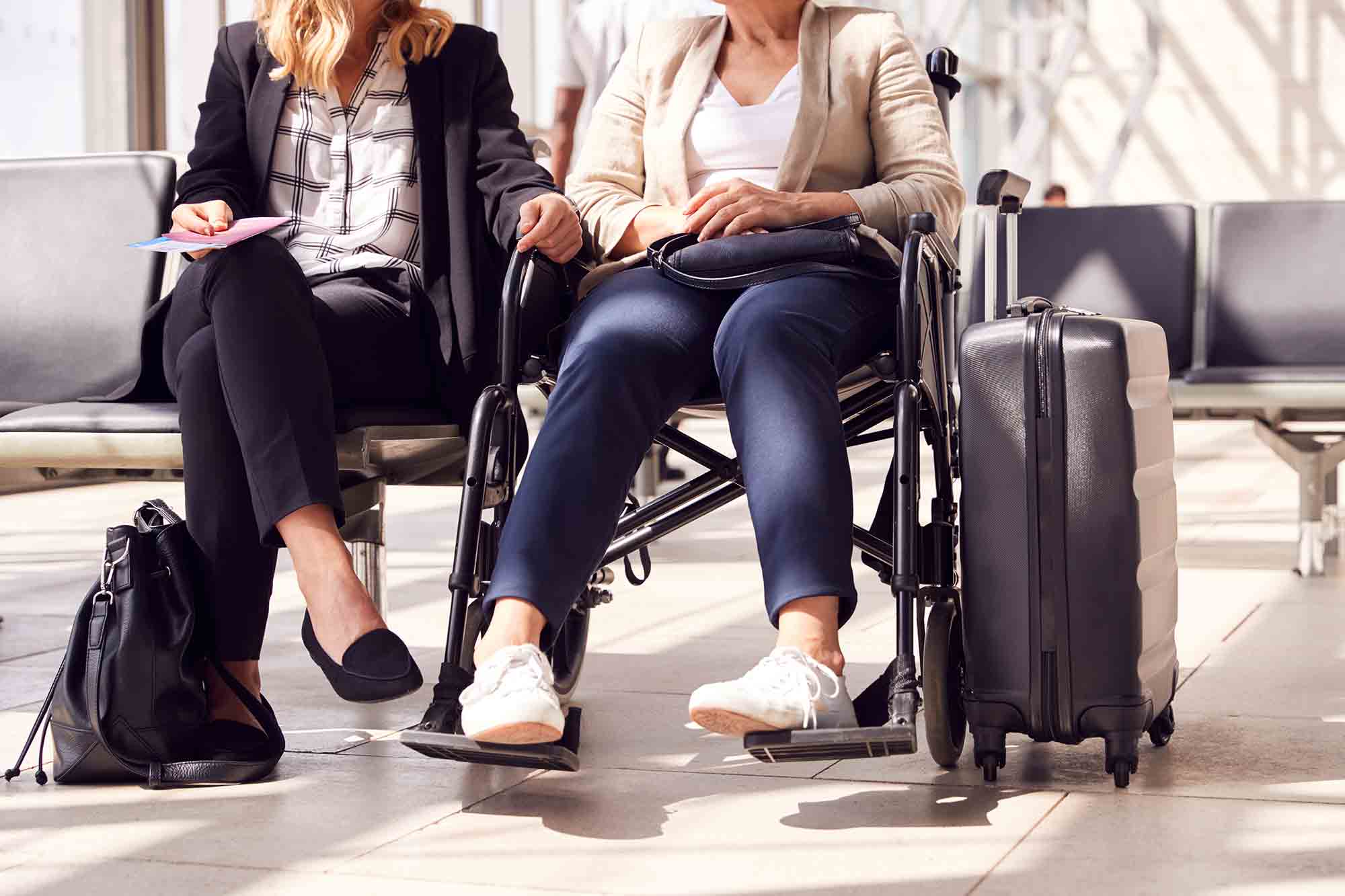 two women sitting in airport one in a wheelchair personal care assistant