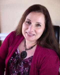 smiling woman sitting in a chair and wearing a burgundy sweater. She is the Disability Diplomat