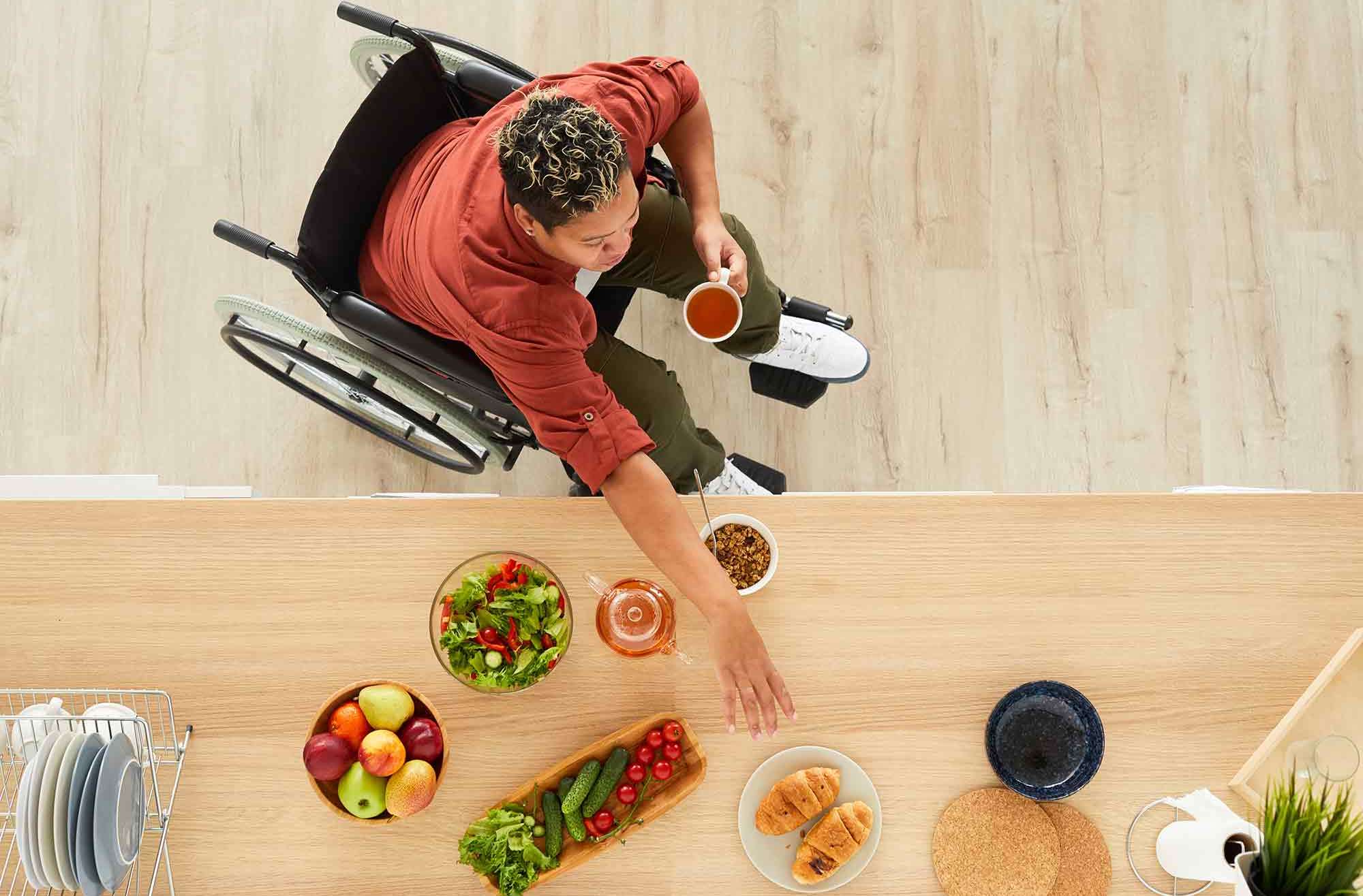 A woman in a wheelchair reaching across a buffet to get food. Demonstrating how there is a need to create food inclusion for individuals with disabilities