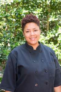 Smiling woman in a black chefs coat standing in front of a tree Chef Educator at Small Bites Adventure Club