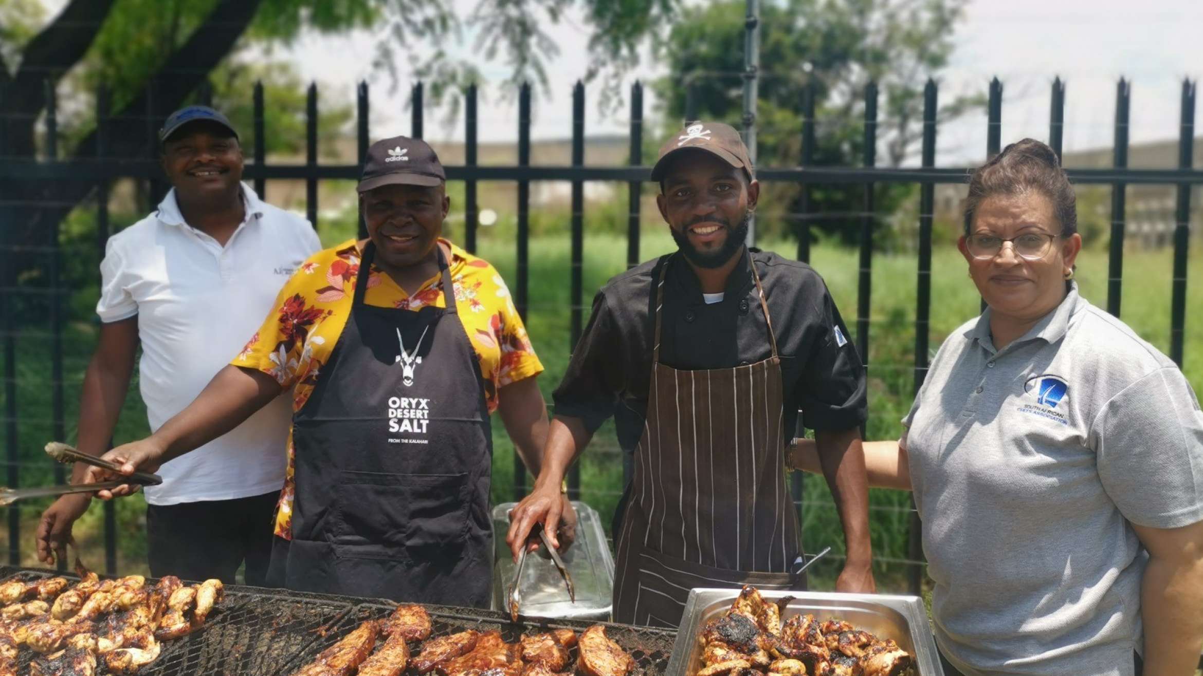 Three men and one standing behind a grill cooking food to give to those in need