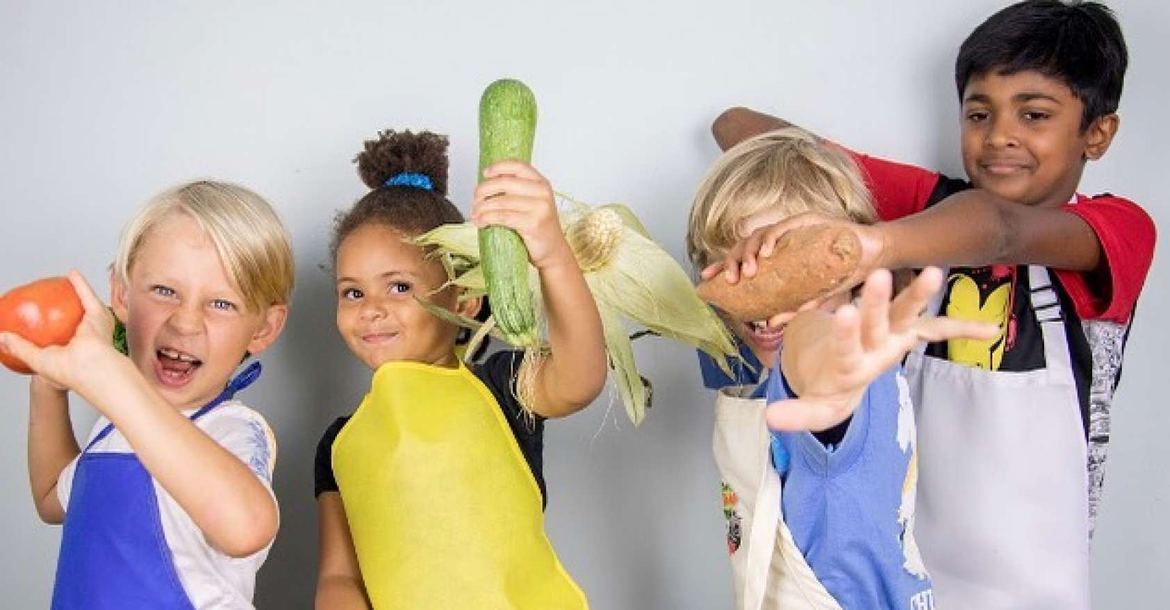 four kids in chef aprons having fun with fruits and vegetables as part of Small Bites Adventure Club