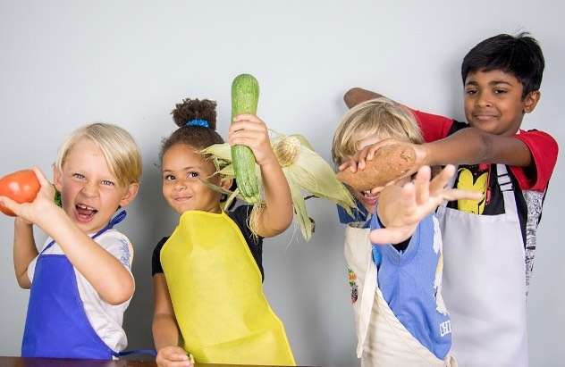 four kids in chef aprons having fun with fruits and vegetables as part of Small Bites Adventure Club