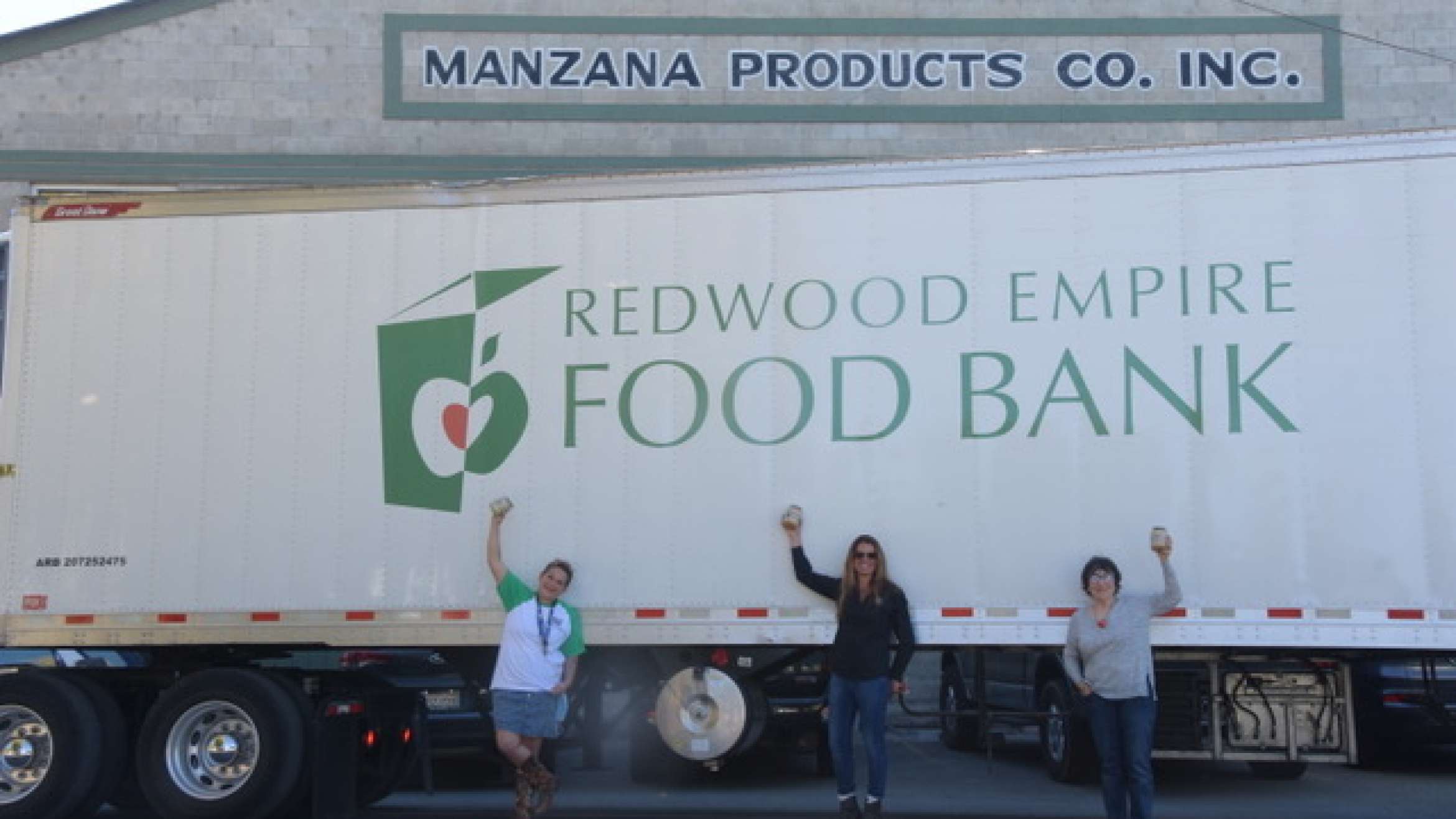 Duskie Estes and two other people standing on the side of a Redwood Empire Food Bank trunk celebrating all of the food they have glean from a local farm