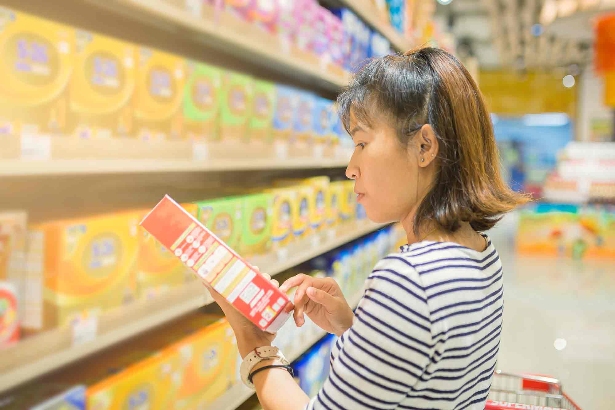 Asian Woman Reading Food label while standing grocery aisle. She managing control of what she eats