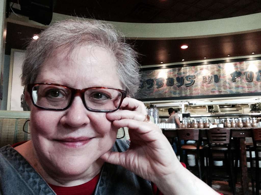 close up of Smiling woman wearing glasses in a restaurant. Her left hand is resting on her left cheek. Safe, Sustainable & Inclusive