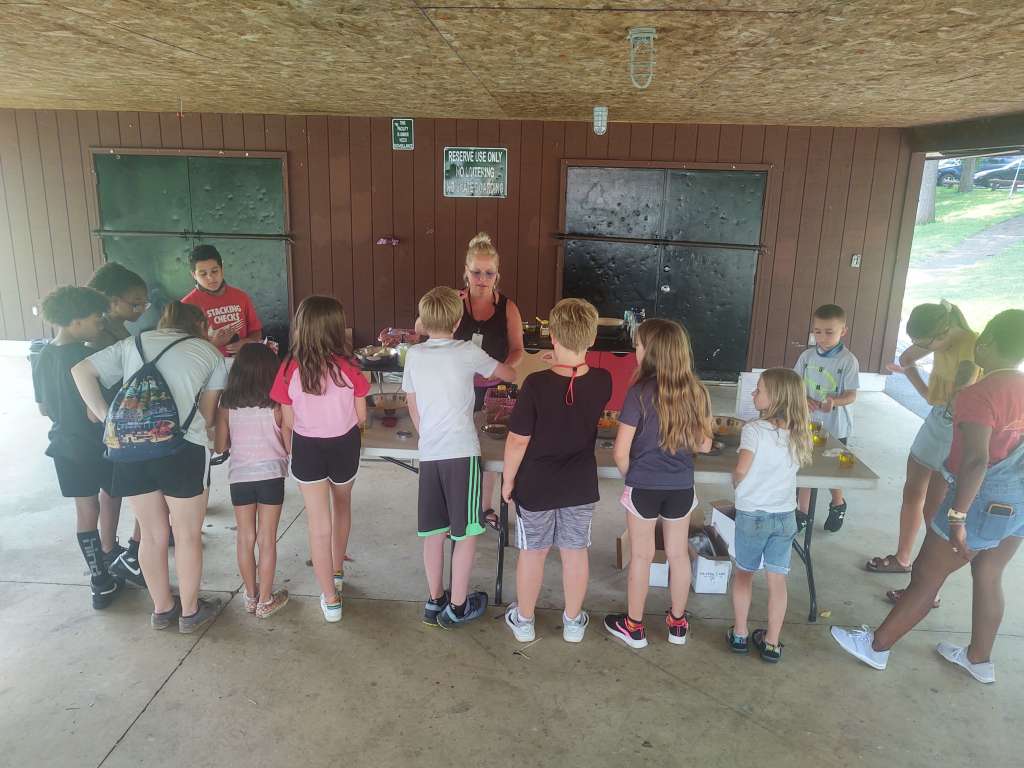 Woman standing in front of a group of kids under an pavillion. She is teaching them nutrition while managing alpha gal syndrome