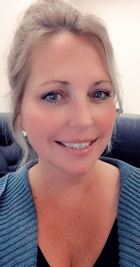 Close up of smiling woman in a blue sweater with her hair pulled back. She has alpha gal syndrome