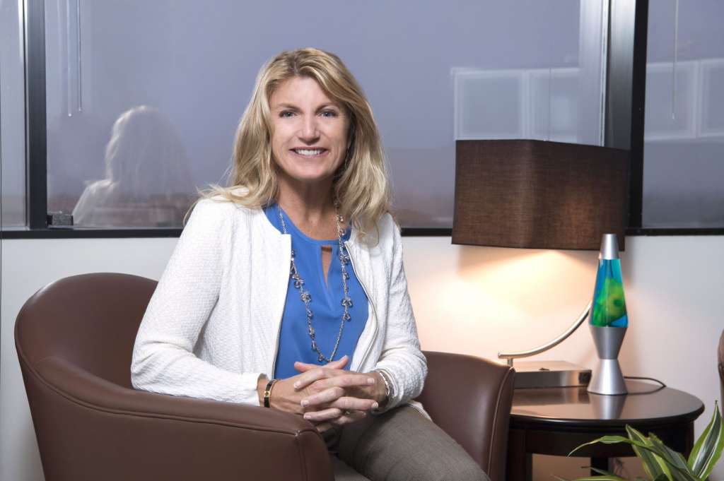 Smiling woman with blonde hair wearing a blue blouse and white cardigan. She is sitting in a chair with her hands clasped. Annette Gregg, MPI WEC