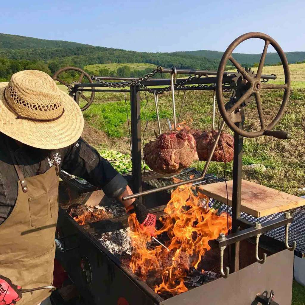 Man grilling meat over an open flame - Brandon Snooks Farm to Fire Catering