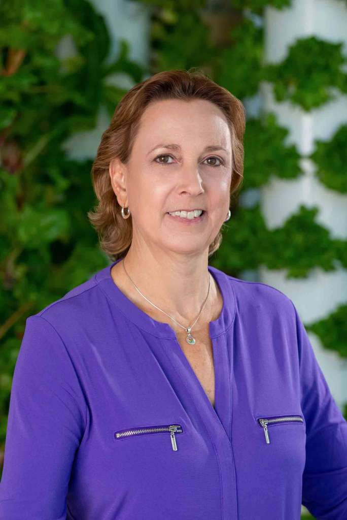 Smiling woman in a purple blouse standing in front of a vertical lettuce wall