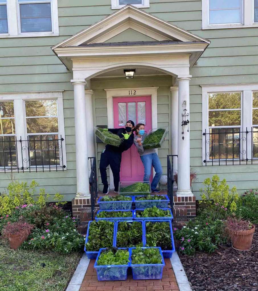 Two people posing on the stoop of a house delivering bins of green vegetables. This delivery one of Sodexho Live!'s ways of is responsible for embedding sustainability into their every day initiatives 