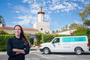 Woman standing in a parking lot. A building and her Made by Meg catering truck are behind her