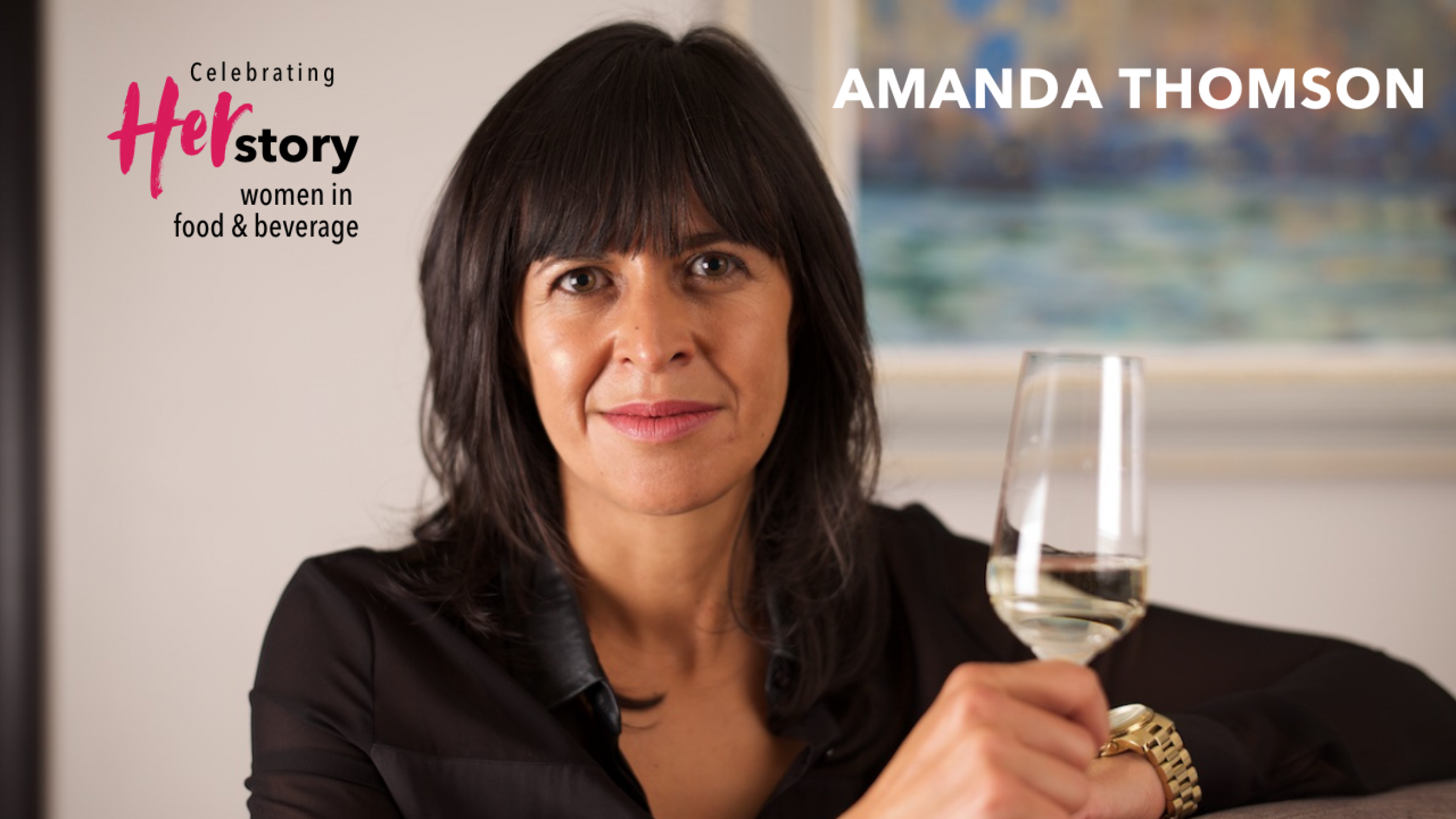 Woman with long dark hair wearing a black shirt leans on a high table while holding a glass of alcohol-free white wine Amanda Thomson, Thomson & Scott, Women Making HERStory with greater transparency in wine labeling.