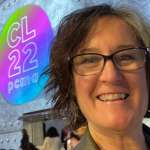 close-up selfie of smiling woman standing in front of a sign on a wall - CL22 PCMA