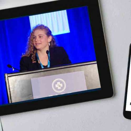An iPad and iPhone on a table. On the iPad is a picture of a young woman standing behind a lectern are on video screen. On the iPhone is the Eating at a Meeting podcast logo with Episode #172 Lobbying for Systemic Change in Food Service with Elise Buellesbach