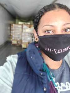 Woman with a mask standing at the entrance of an 18-wheeler track with boxes of rescued food behind her. 