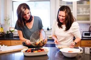 Two women in a kitchen making a fruit pie — Two Alpha Gals
