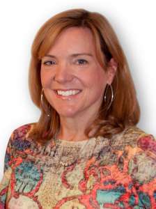 Smiling woman with red hair wearing a colorful blouse and looking at the camera.