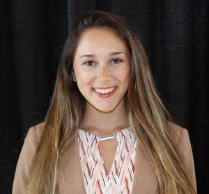 Smiling woman with long brown hair in a brown suit jacket in front of a black wall. Her name is Kayla King, founder of MyMeal