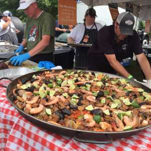 a large skillet of paella with chefs behind it