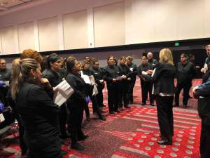 a group of banquet servers being trained by their boss in a large convention center ballroom. She is reminding them of food safety practices