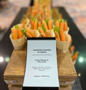Vegetable shooters in paper cones. The buffet label is in front of them, identifying the allergens and dietary needs. An example of good food safety practices.