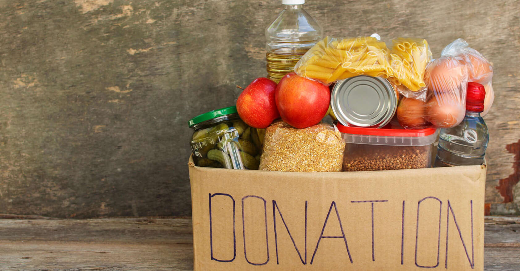 Cardboard box labeled ‘donation’ filled with food items including apples, pasta, canned goods, grains, and bottled water, symbolizing community food drives and surplus food donation.