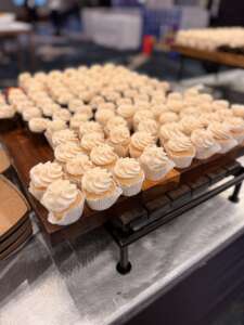 dozens of mini cupcakes with white icing on a wooden platter on a silver table. GLP-1 users like smaller portion sizes 