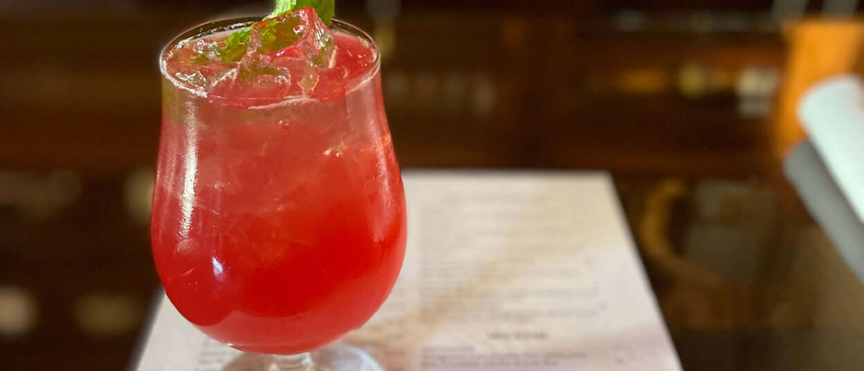 Red zero-proof beverages with a piece of mint. Sitting on top of a menu on a bar