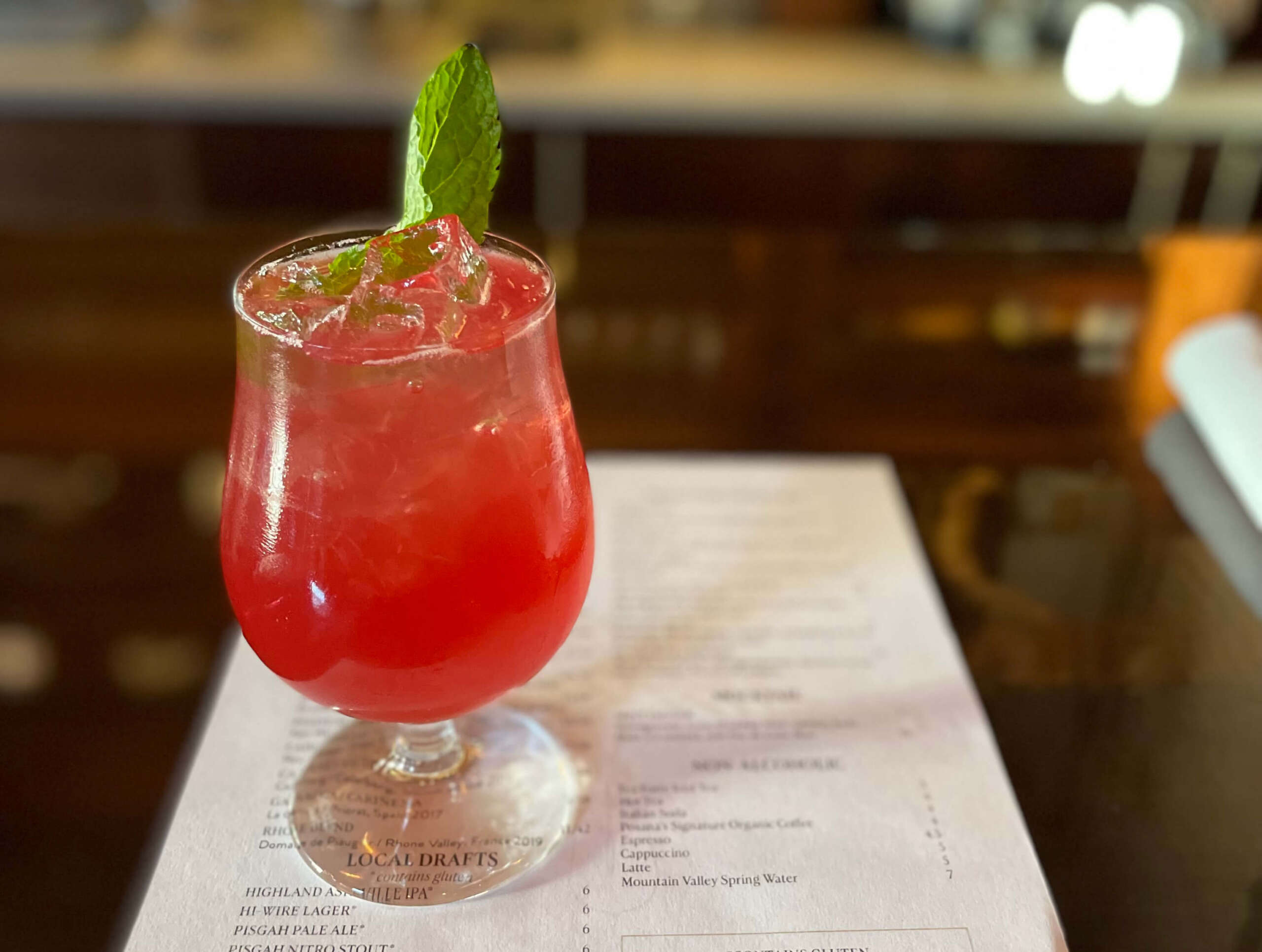 Red zero-proof beverages with a piece of mint. Sitting on top of a menu on a bar