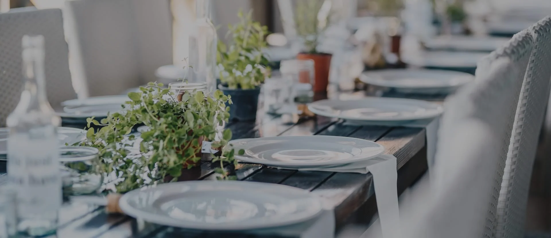 Wooden Table with white plates, napkins and chairs. Small Green plants as center pieces with glass water bottles